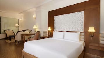 A hotel room with a large bed, a desk, two chairs, and a mirror.