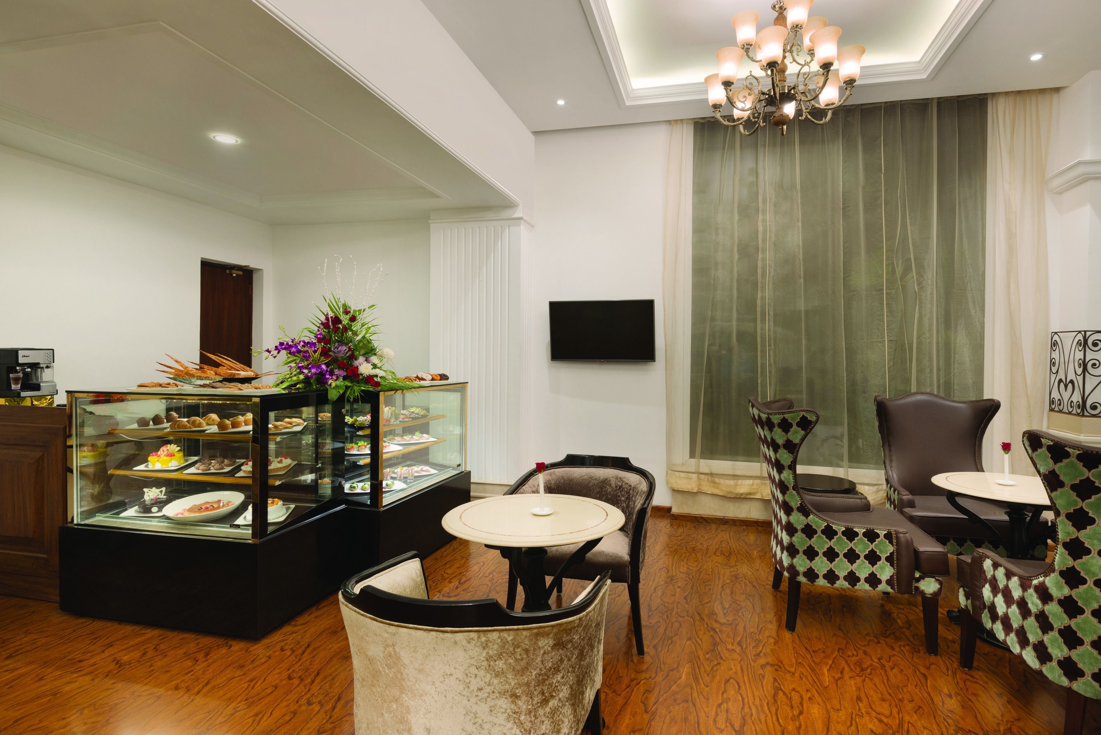 Un hall de hotel con una vitrina de postres, una araña y un televisor en la pared.