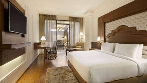 A hotel room with a large bed, a television mounted on the wall, a desk with a chair, and a view of the outside through a door. - Ramada Plaza by Wyndham Chandigarh Zirakpur (Dera Bassi)