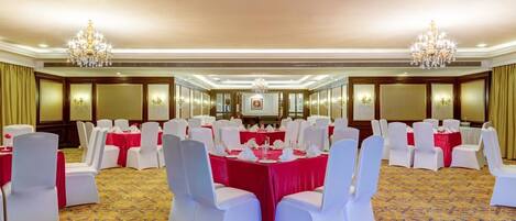A banquet hall with round tables, white chairs, and chandeliers.