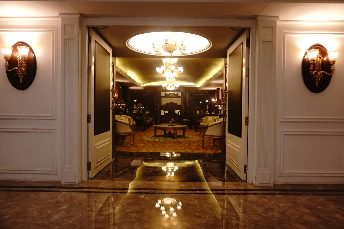 A grand hallway with a reflective floor leading to a seating area with a chandelier.