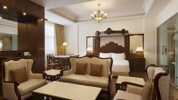 A hotel room with a large bed, a sofa, a dining table, and a chandelier.