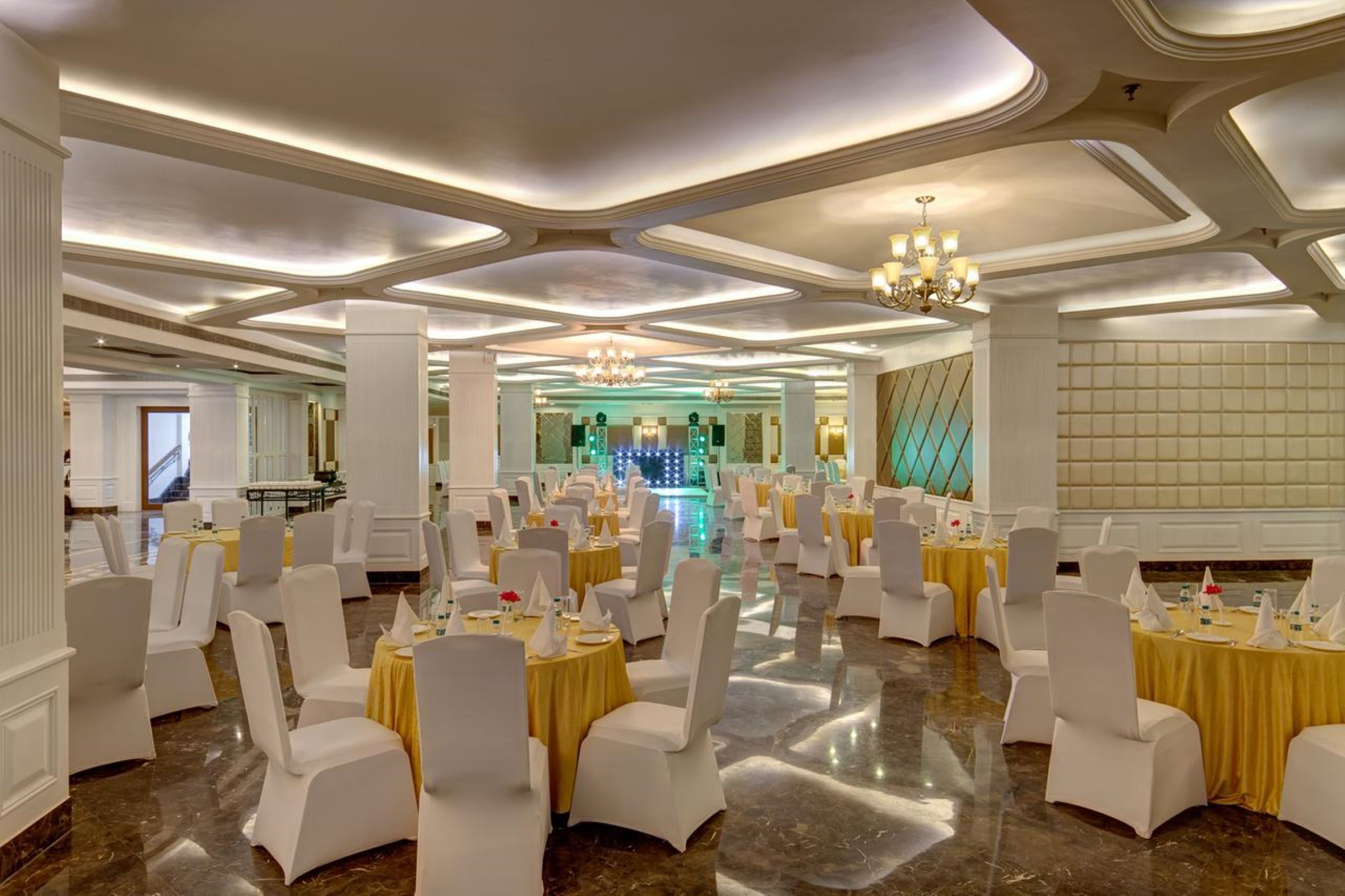 Une salle de banquet avec des tables rondes, des chaises blanches, des lustres et un sol réfléchissant.