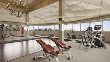 A gym with exercise equipment, benches, and a large chandelier.