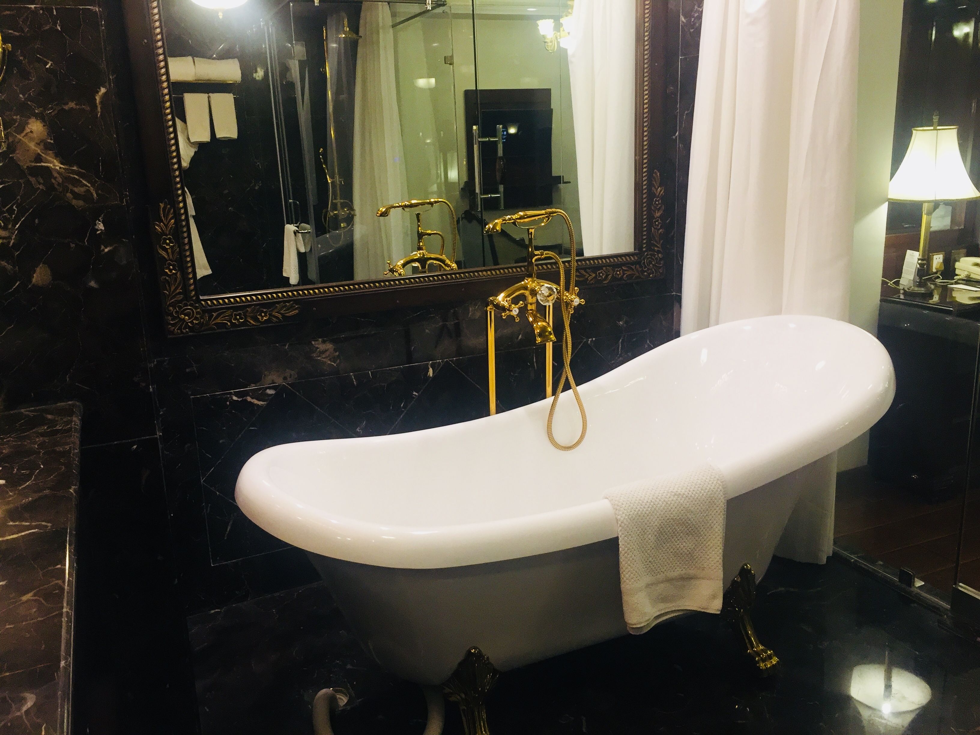 Un baño con una bañera independiente, un espejo grande y un tocador moderno con una lámpara.
