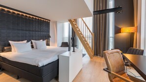 A modern hotel room with a large bed, a desk, a chair, and a staircase. - Leonardo Hotel Groningen Stadspark (Groningen)