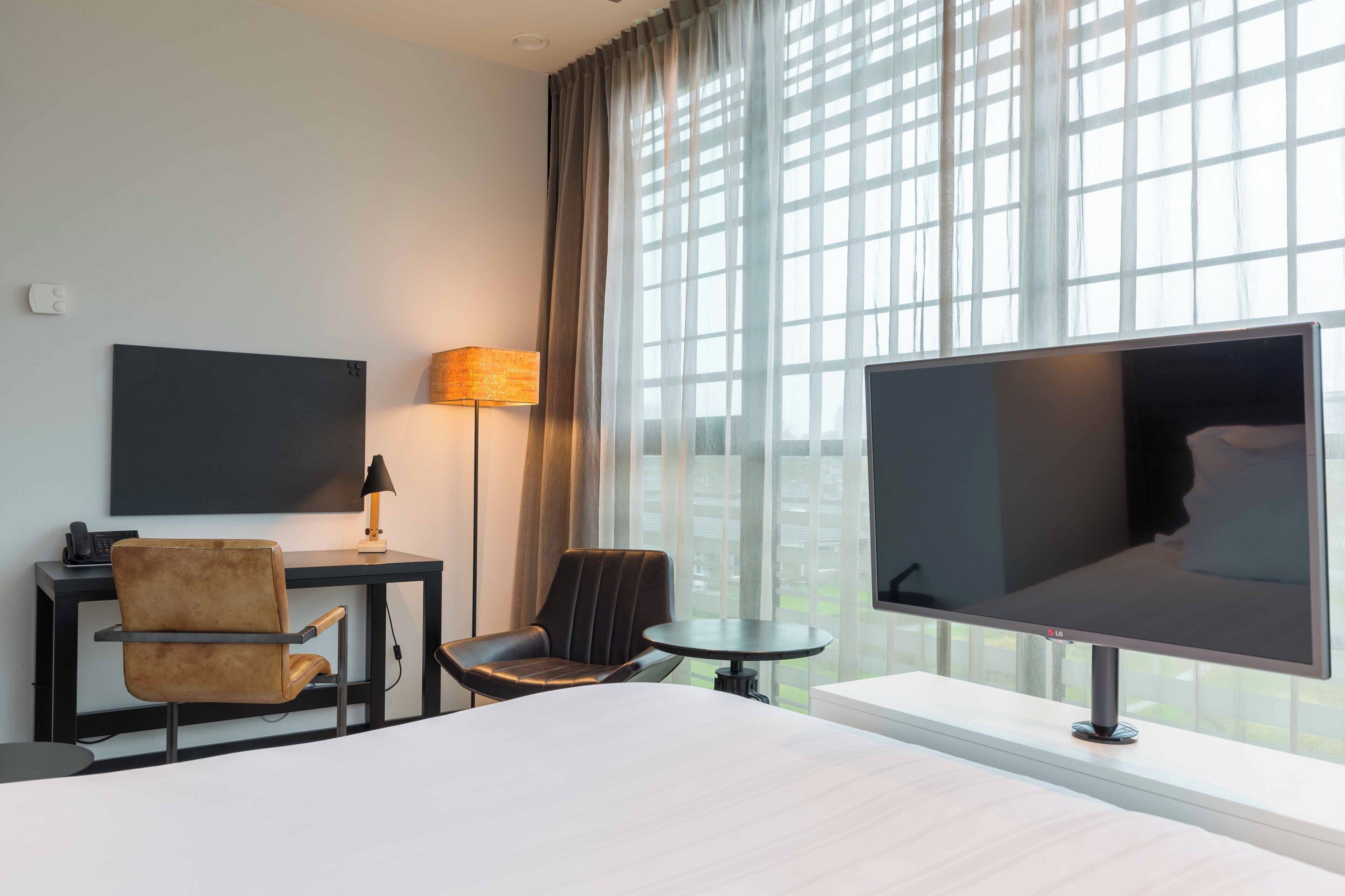Una habitación de hotel con cama, escritorio con lámpara, televisor y una silla.