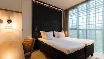 Une chambre d’hôtel moderne, dotée d’un grand lit, d’un bureau en bois et offrant une vue sur la ville grâce à de grandes fenêtres.
