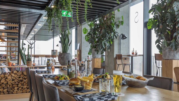 A restaurant with a long wooden table, various dishes, drinks, and hanging plants. - Leonardo Hotel Groningen Stadspark (Groningen)