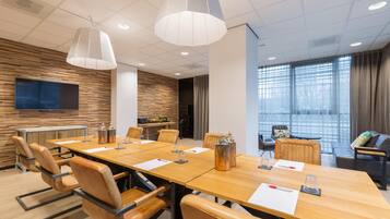 Une salle de conférence avec une longue table, des fauteuils en cuir et un téléviseur fixé au mur.
