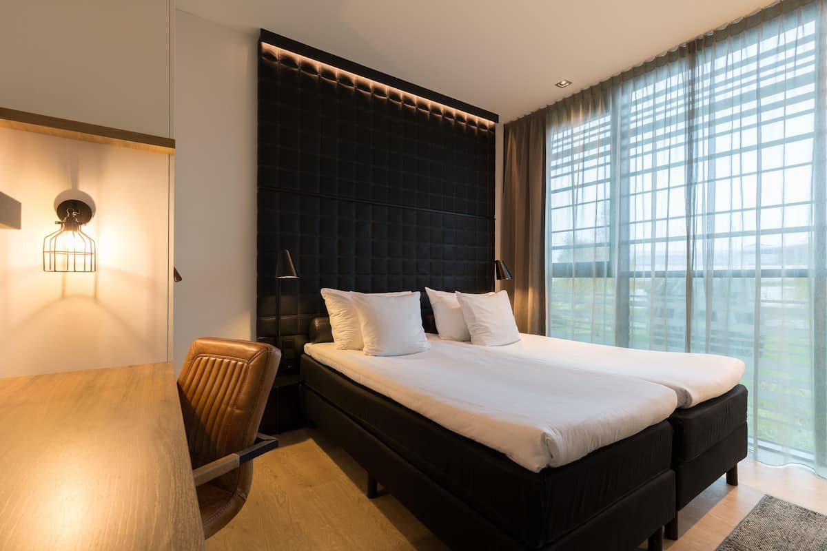 Habitación de hotel moderna con una cama grande, un escritorio de madera y vistas de la ciudad a través de amplios ventanales.