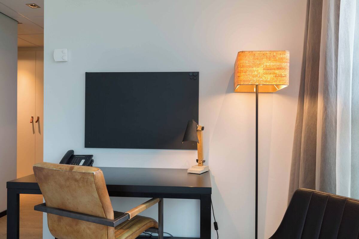 Habitación de hotel con escritorio, silla, televisor de pantalla plana, lámpara y teléfono.