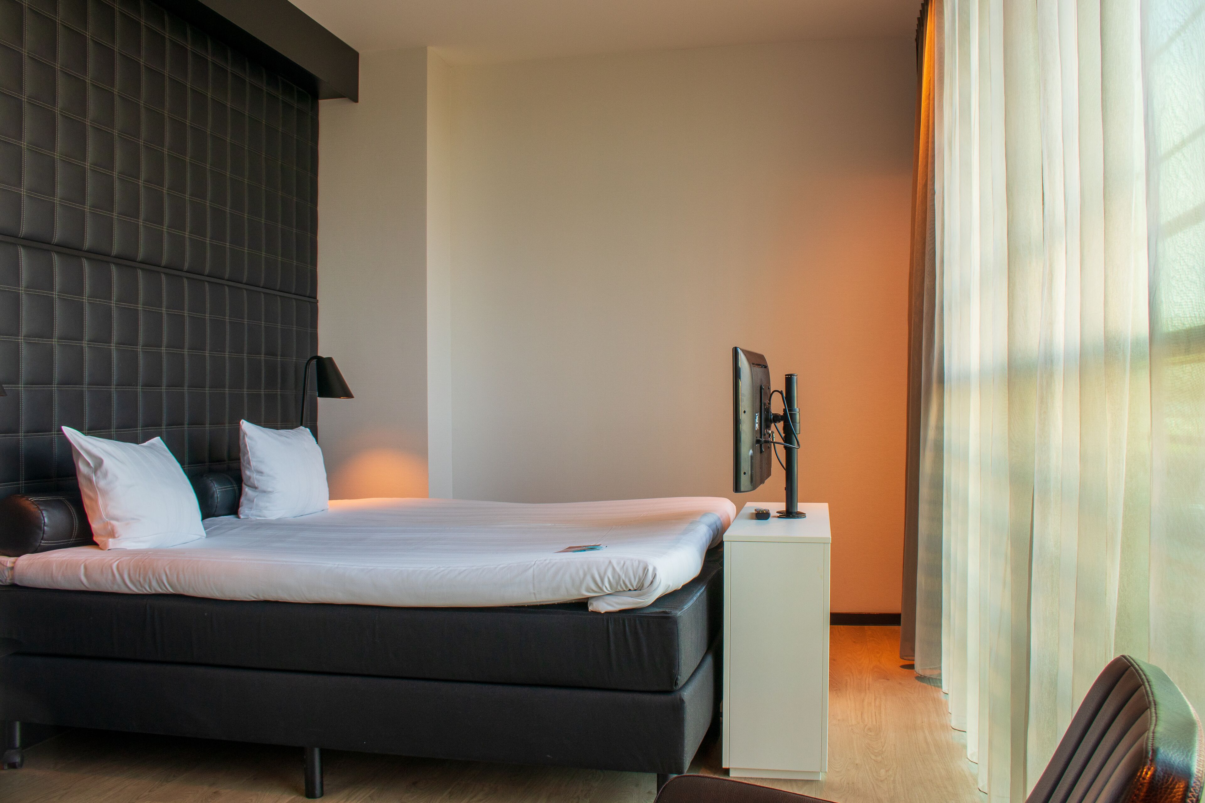 Ein modernes Hotelzimmer mit einem großen Bett, einem Flachbildfernseher auf einem Schrank und einem Fenster mit Vorhängen.