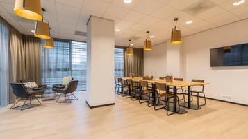 Uma sala de conferências moderna com uma mesa comprida, cadeiras e iluminação pendente.