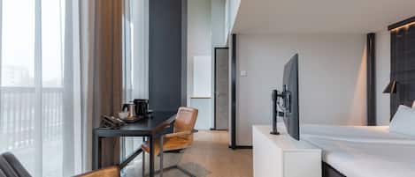 A modern hotel room with a bed, a desk, a chair, a television, and a window with curtains.