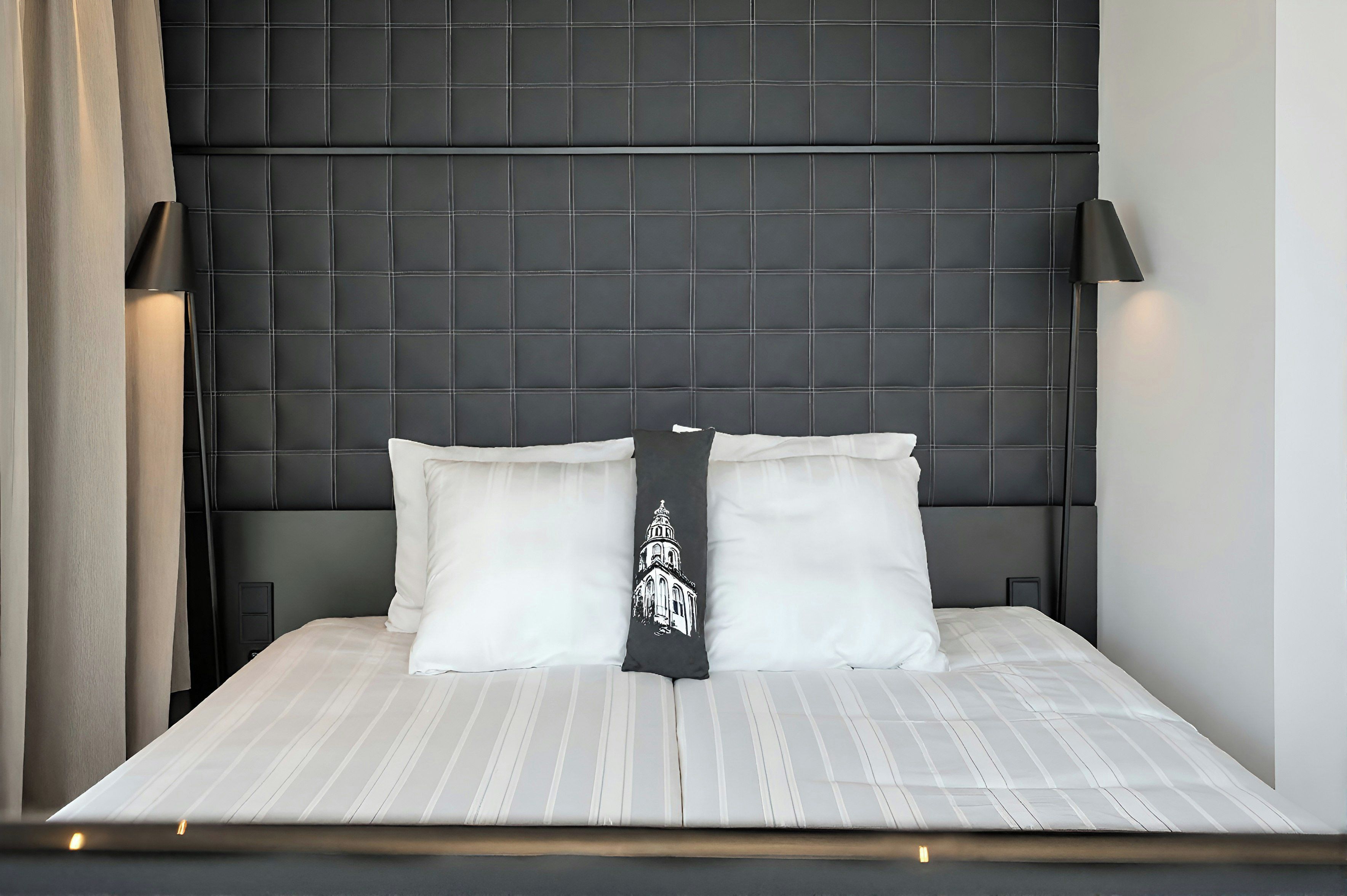 A bed with a headboard featuring a grid pattern, two pillows, and a bedside lamp.