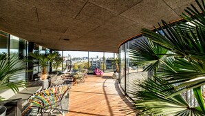A spacious balcony with a wooden floor, seating areas, and large windows offering a city view. - Leonardo Hotel Groningen Stadspark (Groningen)