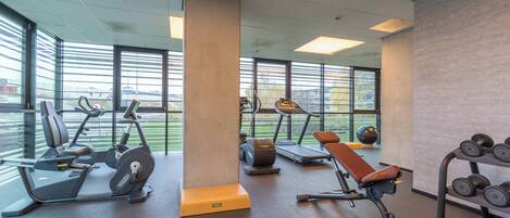 Un gimnasio con equipo de ejercicio, ventanas amplias y vistas al exterior.