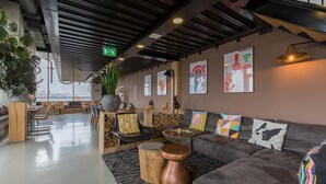 A modern lounge area with a sofa, coffee table, and chairs. There is a staircase in the background, a green exit sign, and a wall with framed artwork. - Leonardo Hotel Groningen Stadspark (Groningen)