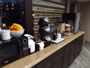Una barra de desayuno con una máquina de café, un bol de fruta y una vitrina con pasteles.