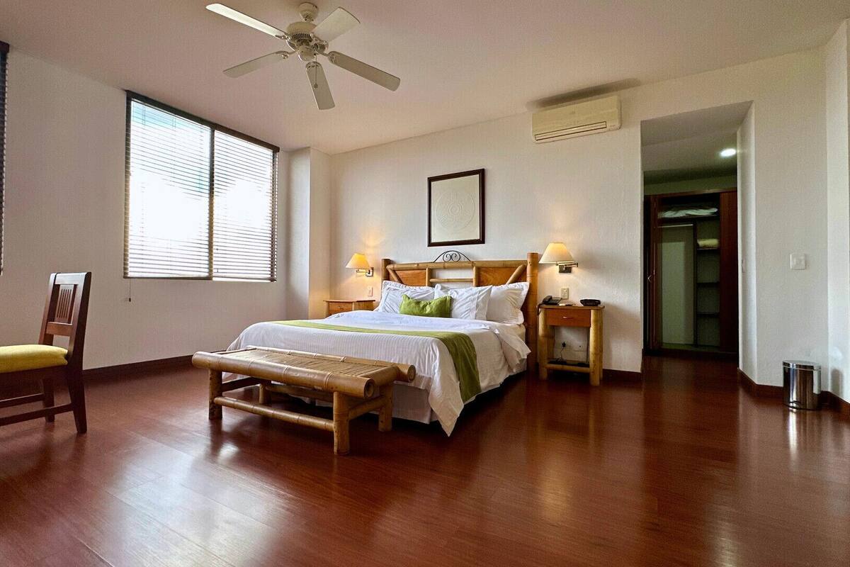 A bedroom with a bed, bedside tables, a chair, a ceiling fan, and a window.