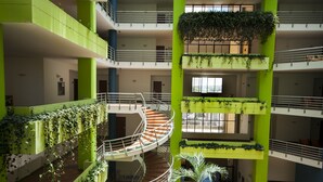 Un atrium à plusieurs niveaux, doté de piliers verts, d’un escalier central en spirale et de plantes suspendues.