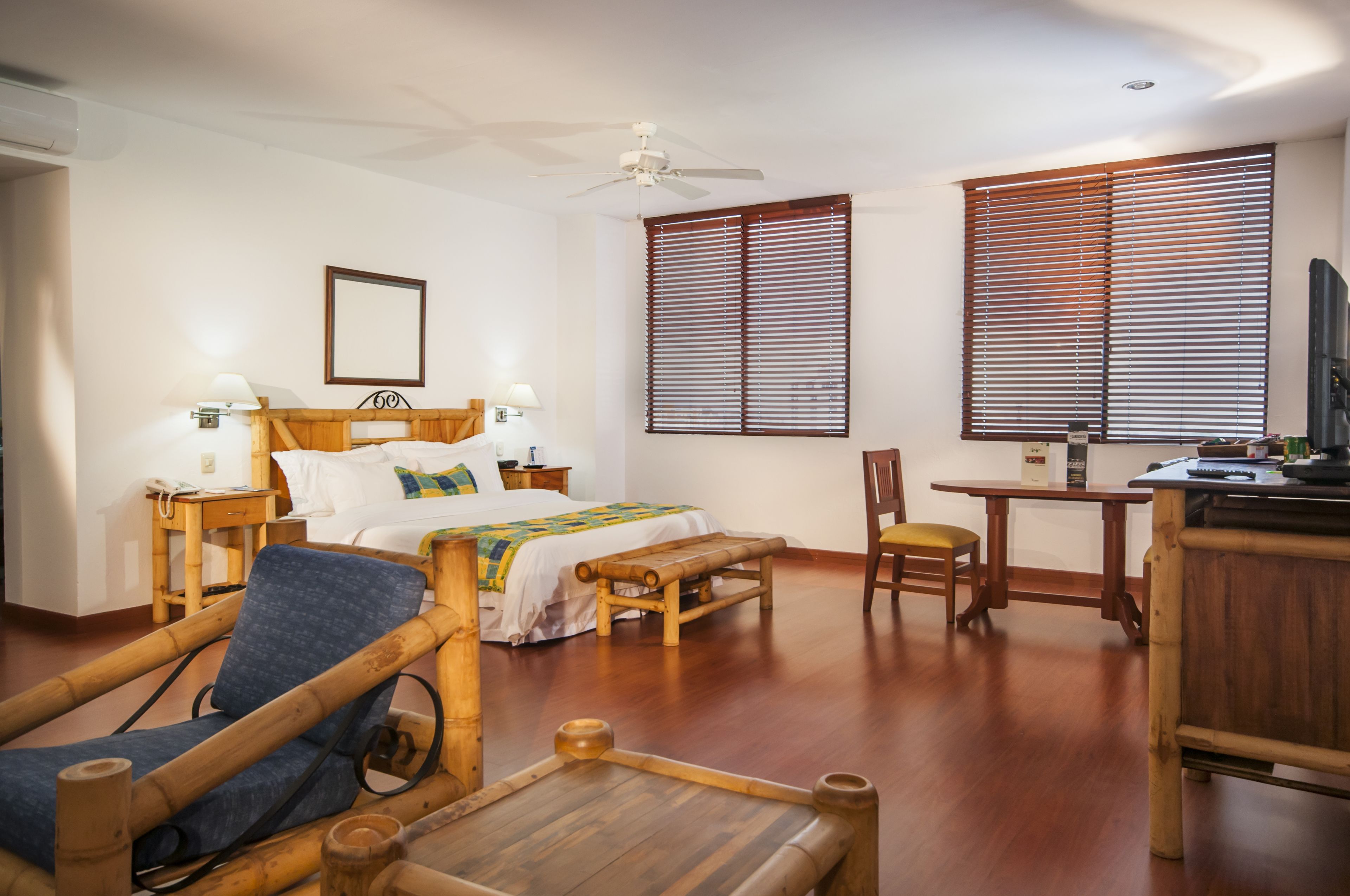 A hotel room with a bed, bedside tables, a desk, a chair, a television, and a ceiling fan.