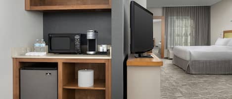 A hotel room with a kitchenette, a bed, and a television.