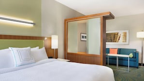 Habitación de hotel con una cama grande, una mesita de noche, una lámpara, un espejo, un sofá y un cuadro en la pared.
