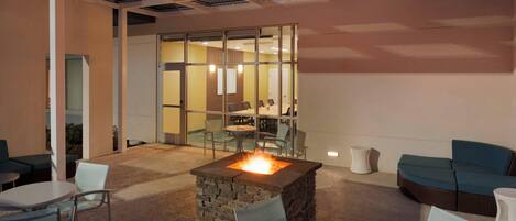 A modern indoor lounge with a stone fire feature, glass partitions, and comfortable seating areas.