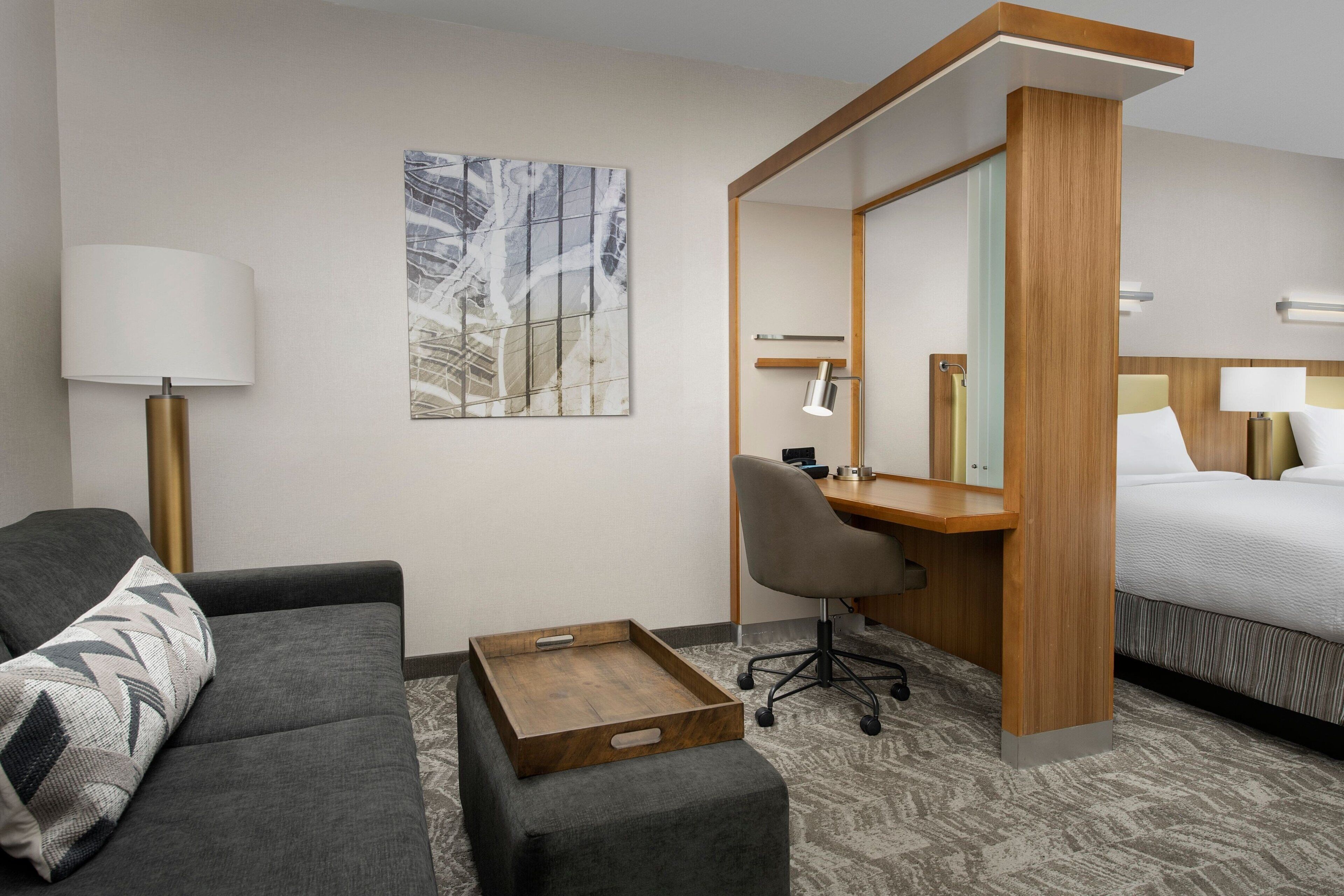 A hotel room with a bed, a desk, a chair, a sofa, a lamp, and a tray.