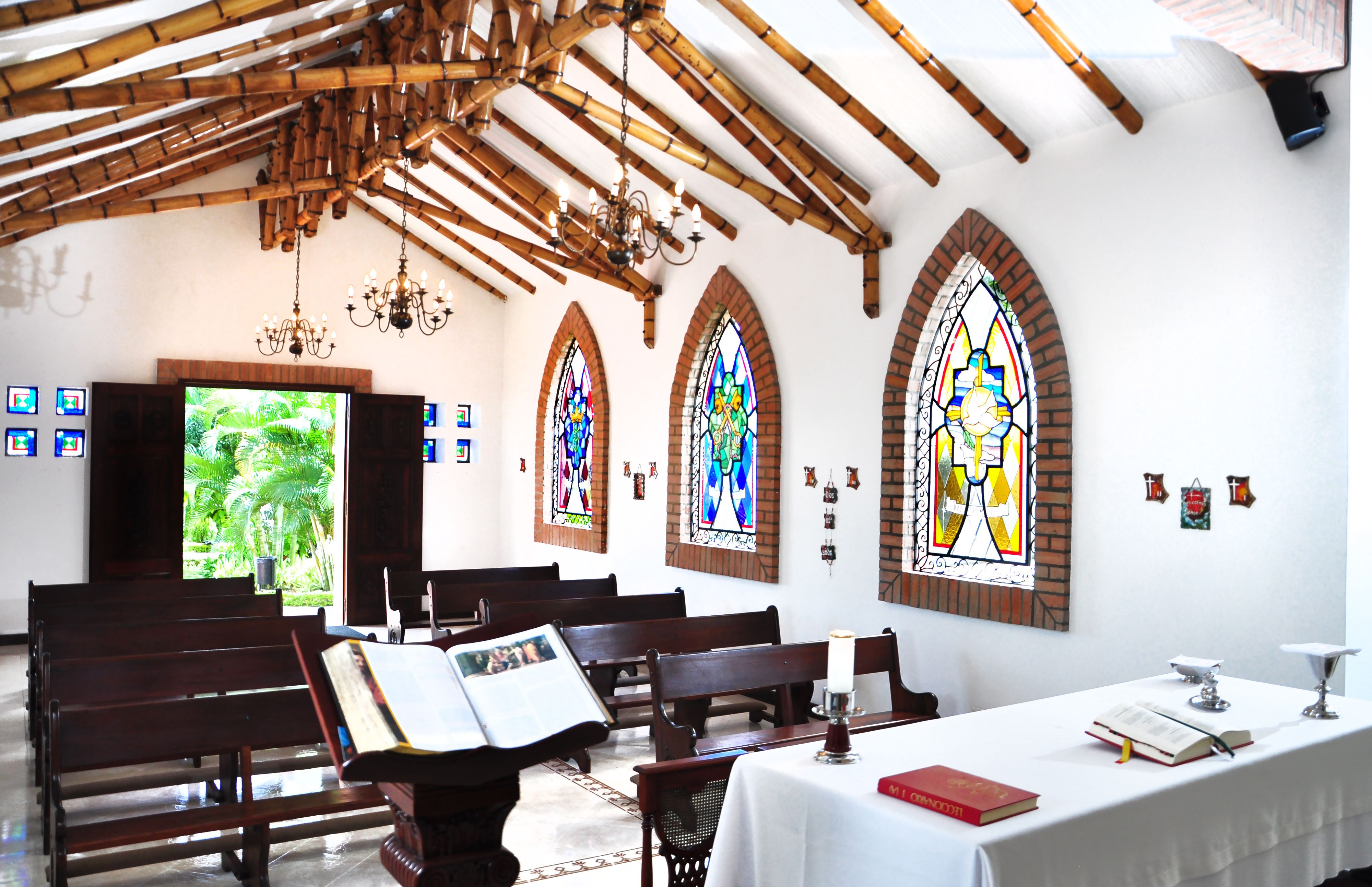 Interior de iglesia con bancos de madera, vidrieras y un altar blanco.