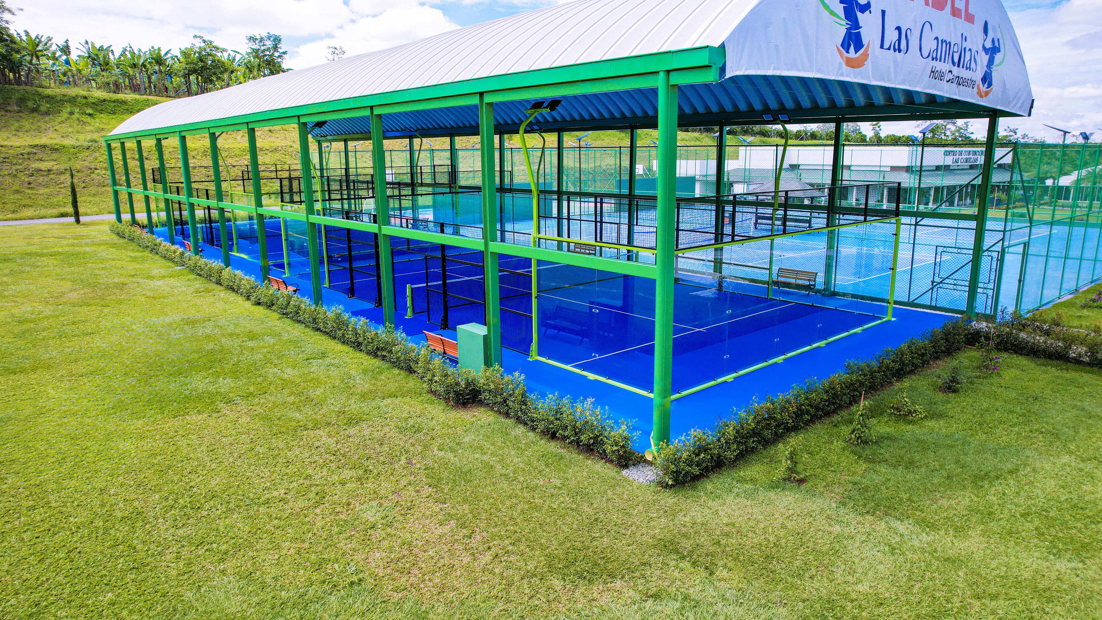 Una piscina techada con estructura verde y parte interior azul, rodeada de césped.