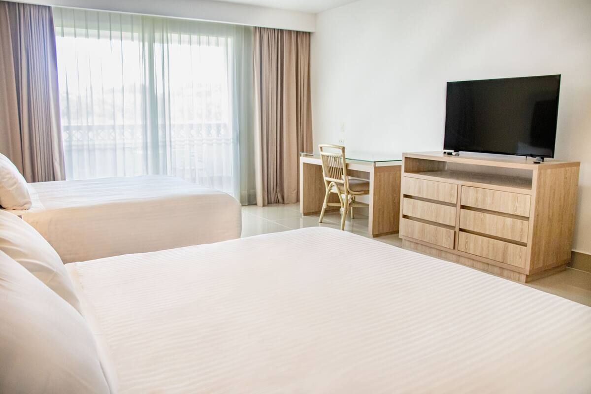 Una habitación de hotel con dos camas, un escritorio, una silla y un televisor.