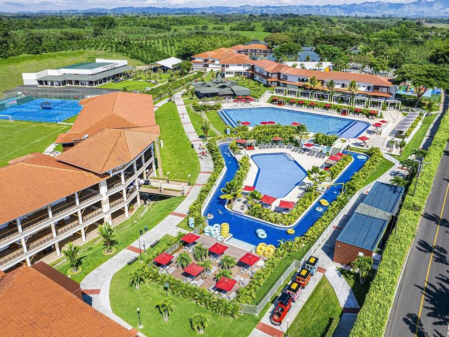 Un complejo turístico con varias piscinas, una cancha deportiva y diversos edificios con tejados rojos.