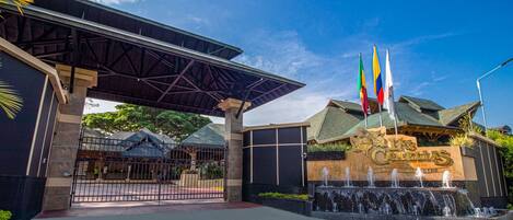 A hotel entrance with a covered walkway, a signboard, and multiple flags.