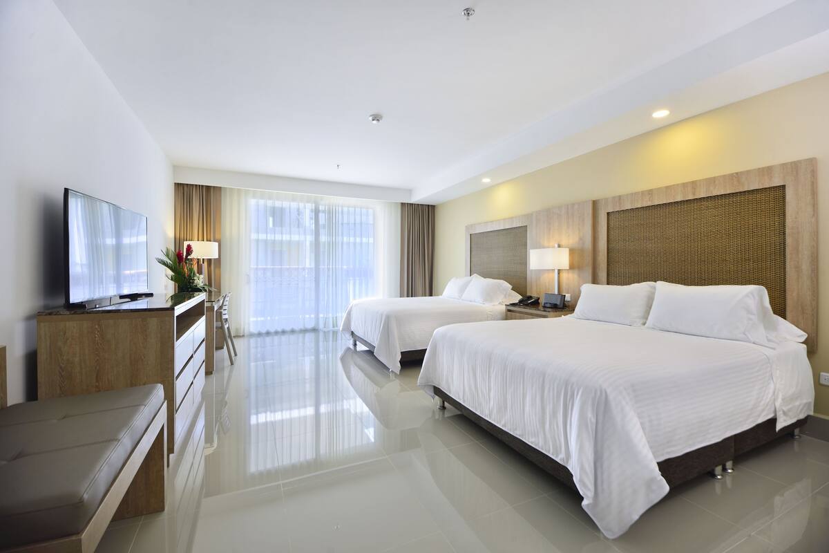 Habitación de hotel con dos camas, televisión, escritorio y un ventanal grande.