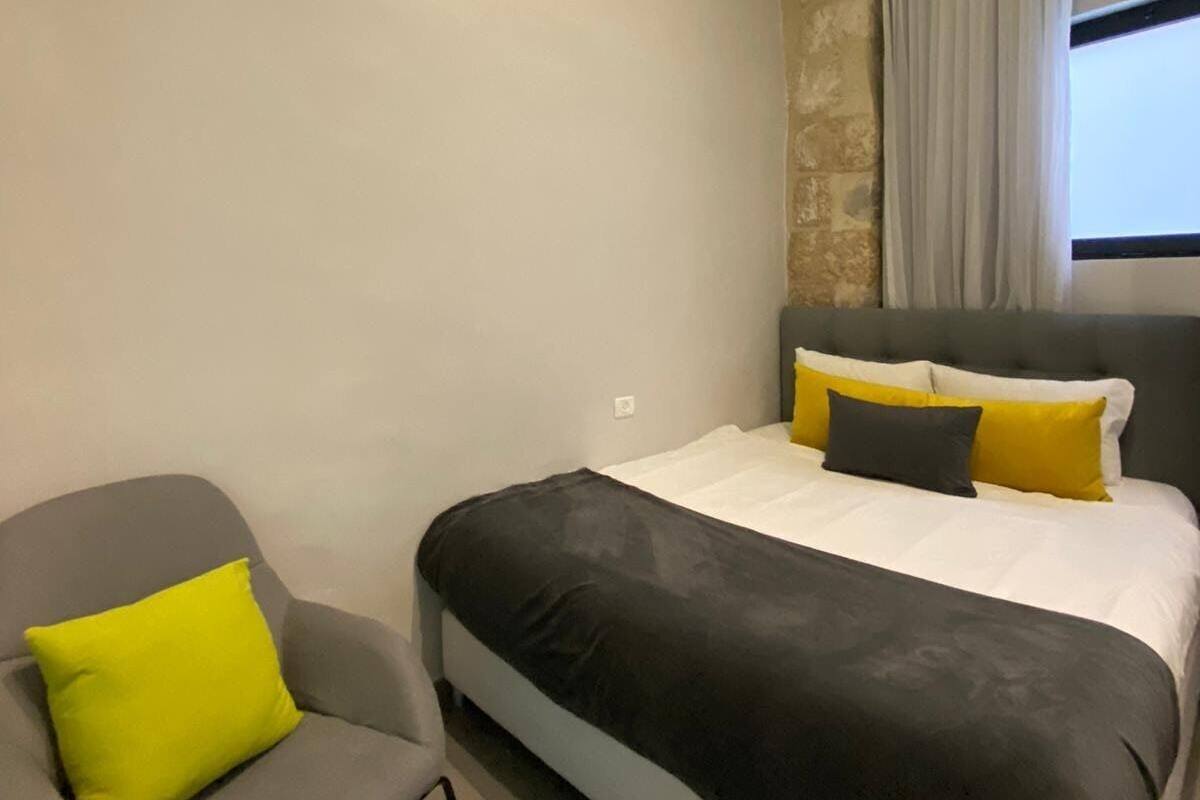 A bedroom with a bed, a chair, a window with curtains, and an air conditioning unit.