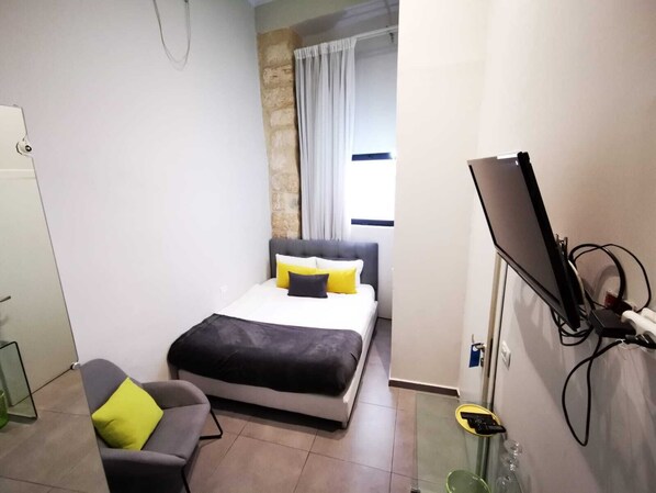 A bedroom with a bed, a chair, a TV, and a window with curtains.