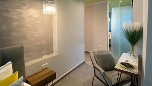 A modern hotel room with a bed, a small table with a vase, a chair, and a green trash bin. - Central Boutique Hotel (Jerusalem)