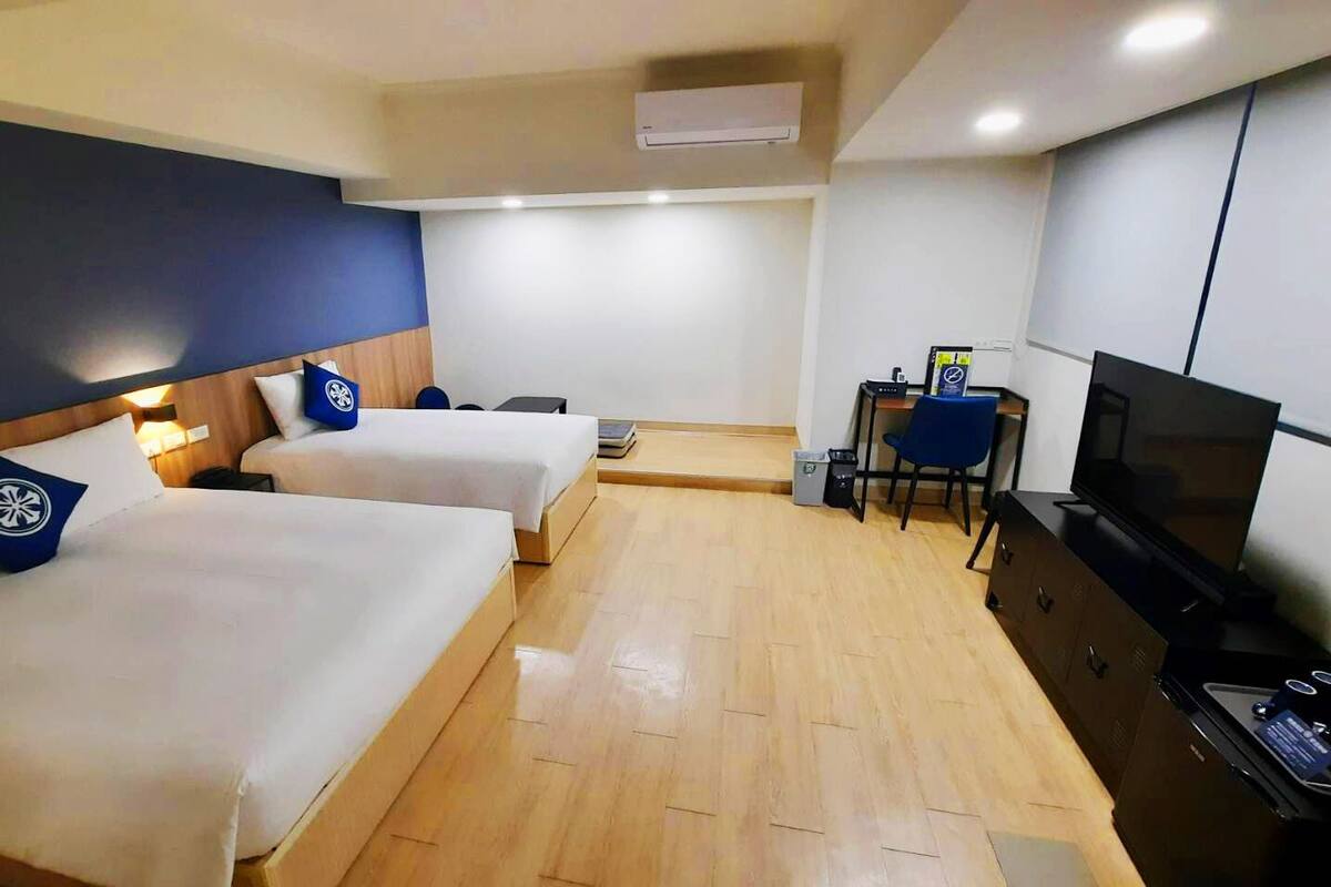 A hotel room with two beds, a desk with a chair, a TV, and a small table.