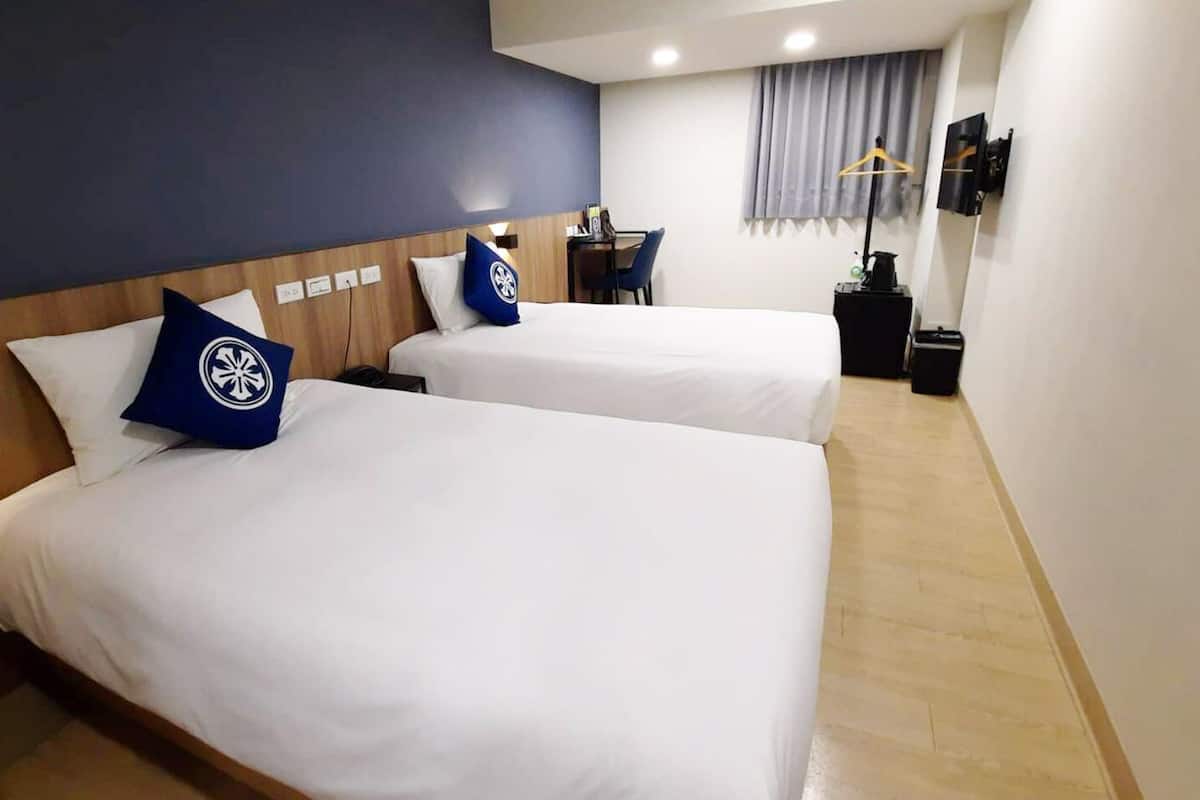 A hotel room with two beds, a desk, a chair, a TV, and a window with curtains.