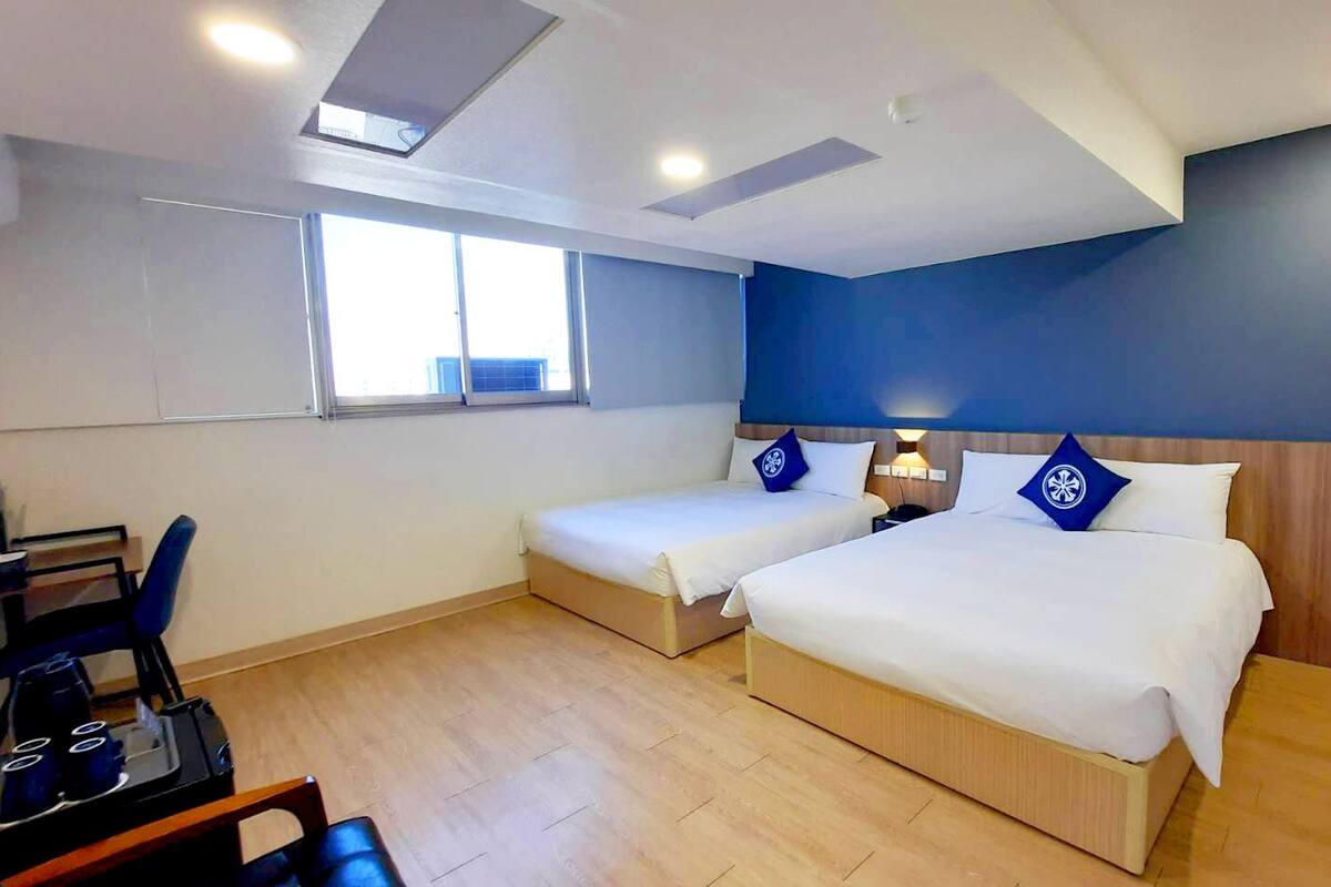A hotel room with two beds, a desk, and a chair.