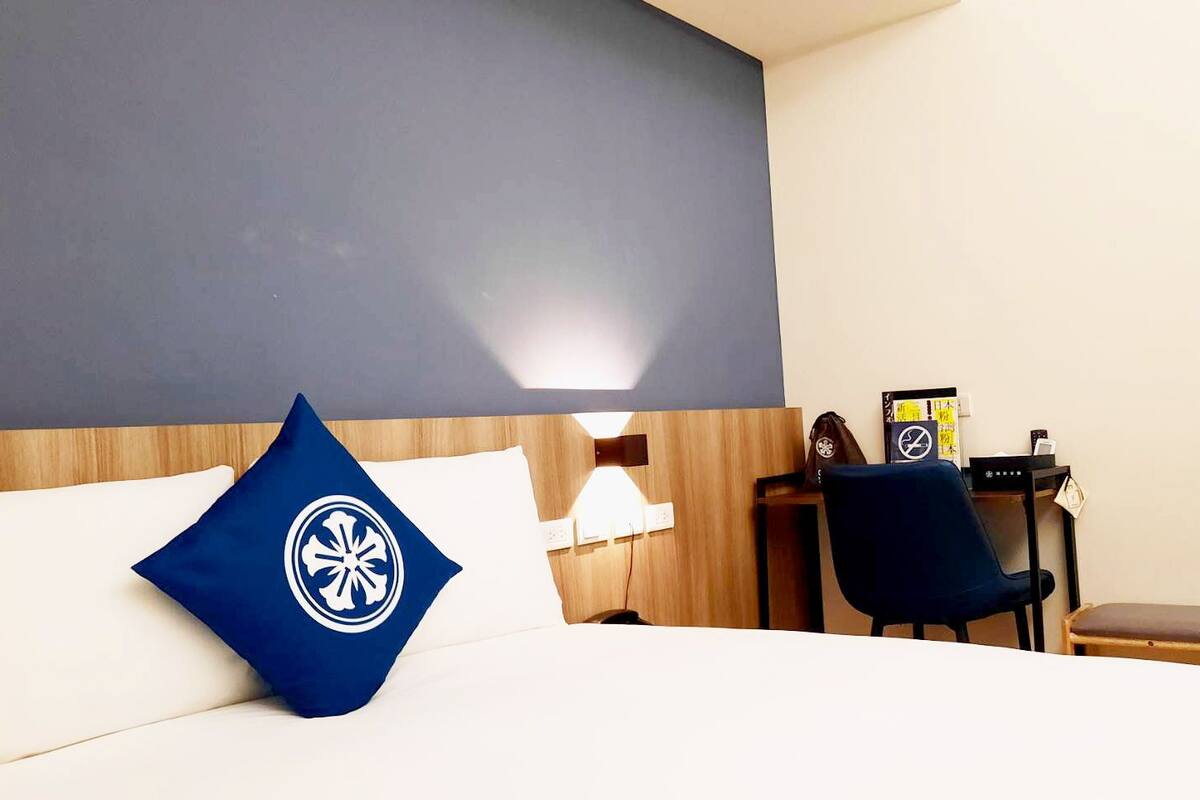 A hotel room with a bed, a desk, a chair, and a bench.