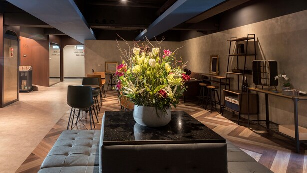 Un interior moderno con un arreglo floral central sobre una mesa negra, rodeado de asientos y una escalera.