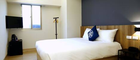 A hotel room with a bed, a TV mounted on the wall, a coat rack, and a small table.