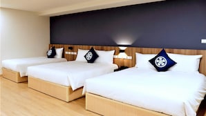 Habitación de hotel con tres camas individuales, cada una con cabecero de madera y ropa blanca.