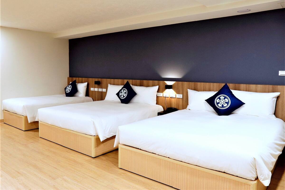 A hotel room with three single beds, each with a wooden headboard and white bedding.