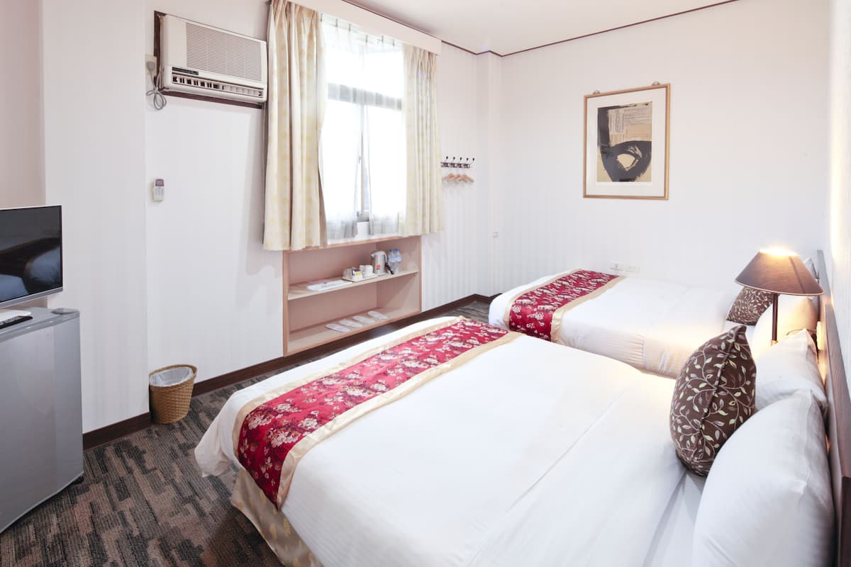 A hotel room with two beds, a television, a shelf with toiletries, and a framed picture on the wall.