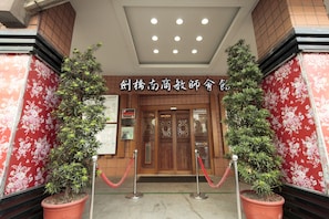 A hotel entrance with a red floral wall, a wooden door, and two potted plants. - Cambridge Confucius Inn (Tainan)